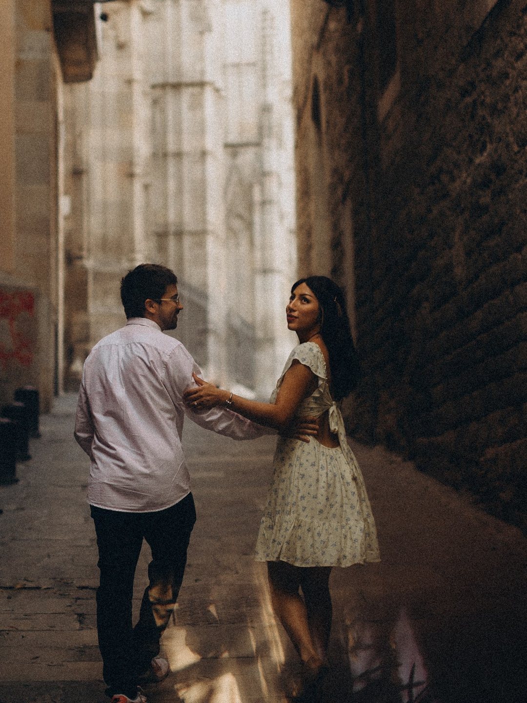 David y Banellye caminando por un callejón de piedra; ella voltea hacia atrás y sonríe